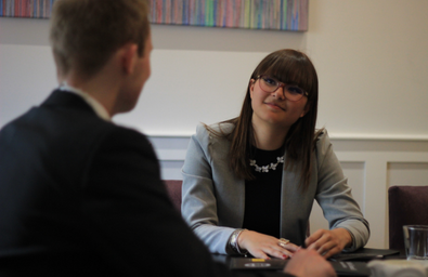 A photo of two people in a discussion, one person is smiling while listening to the other person talking