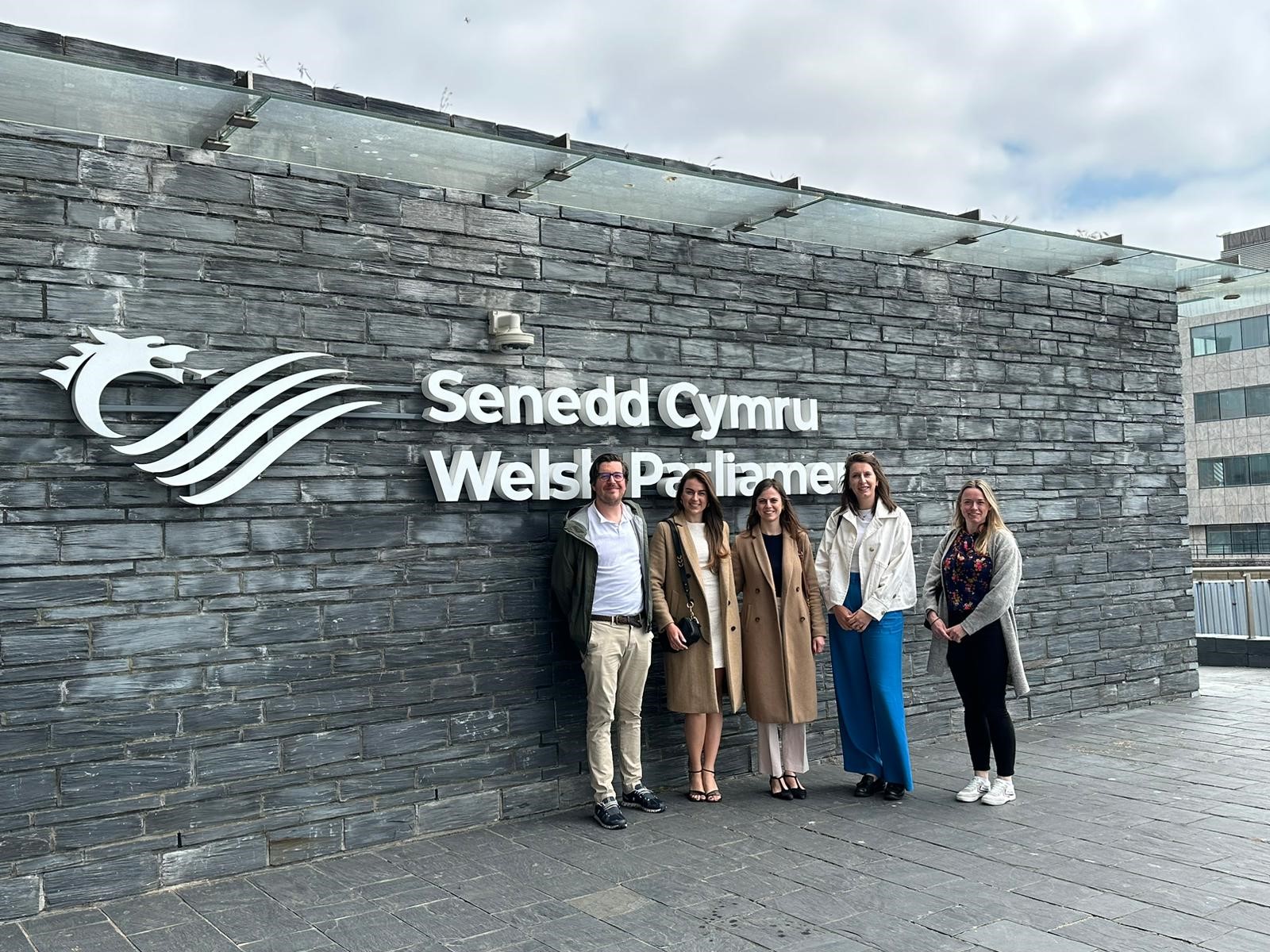 Five smart casually dressed people stood outside the Welsh Parliament building