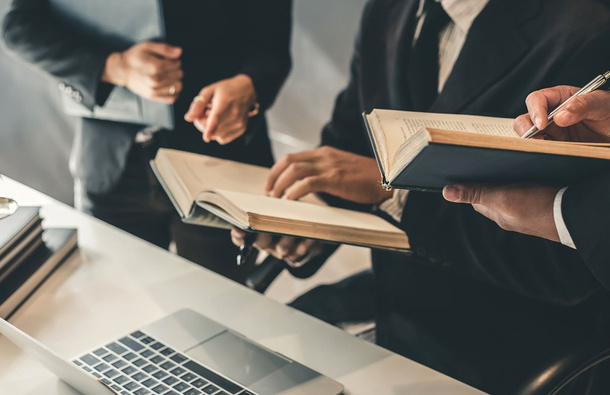 Lawyers holding notebooks around a desk.